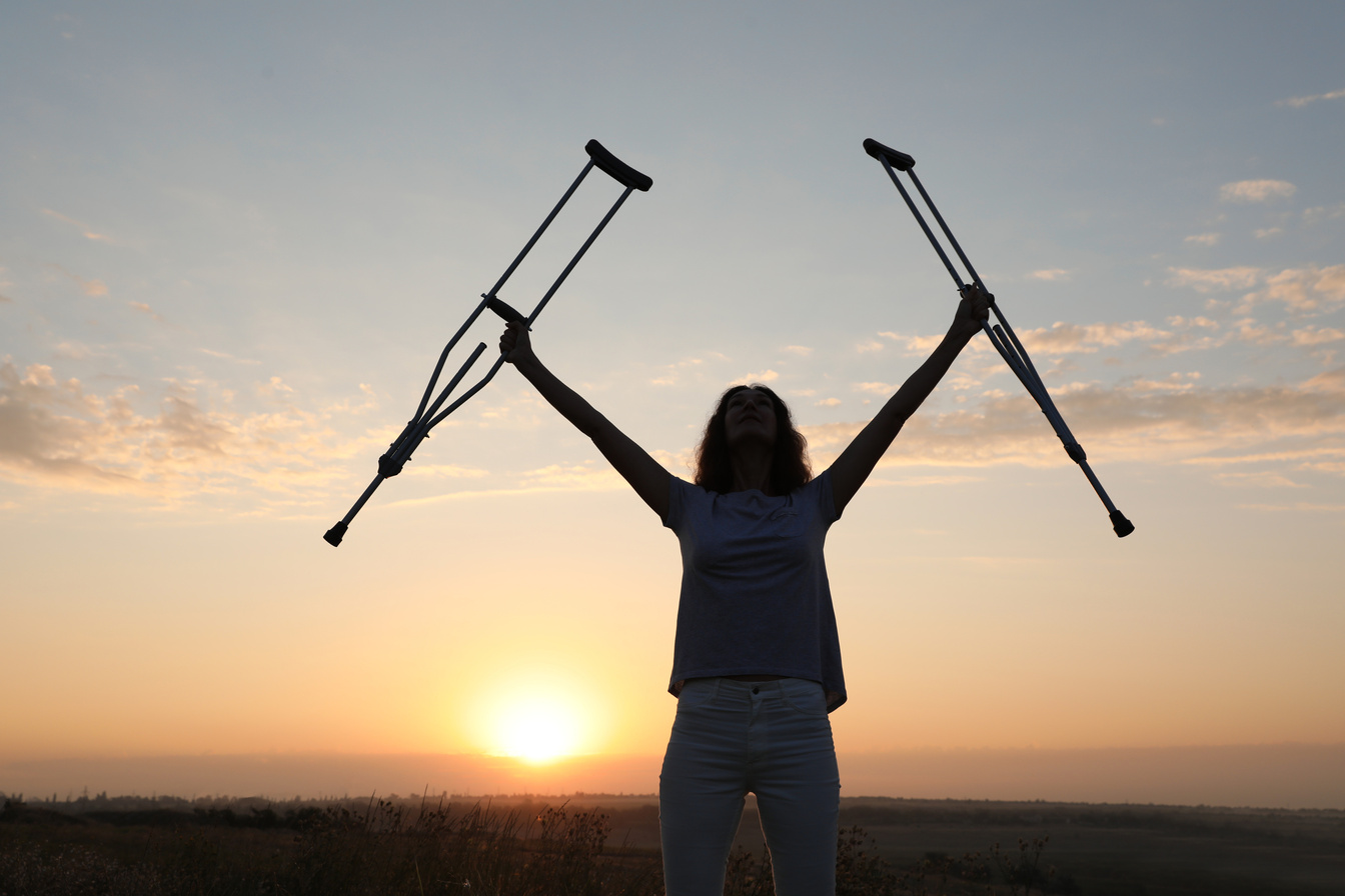 Woman Holding Axillary Crutches Outdoors at Sunrise. Healing Miracle